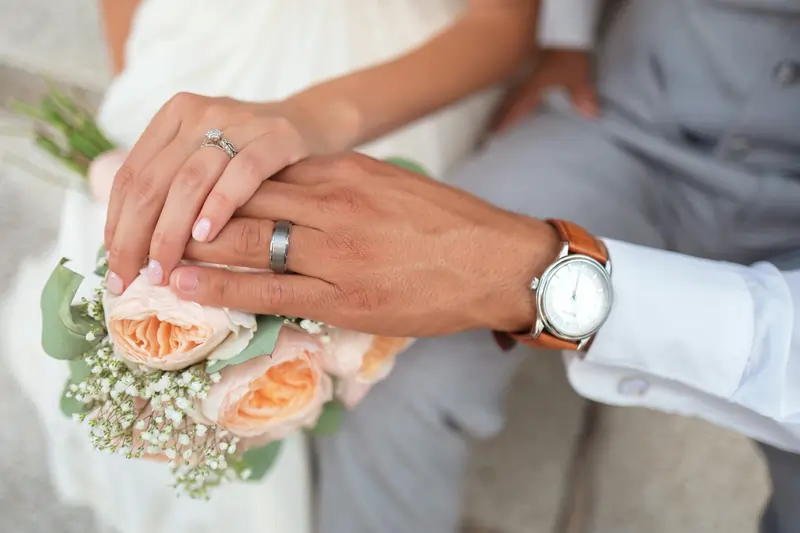 A couple with rings touching flowers together on their wedding day.